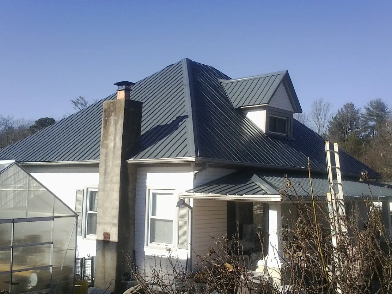 Dark blue standing seam metal roof on a white farmhouse with dormer — Slate & Tile Roof Repair by Roofing Brothers in Highmount