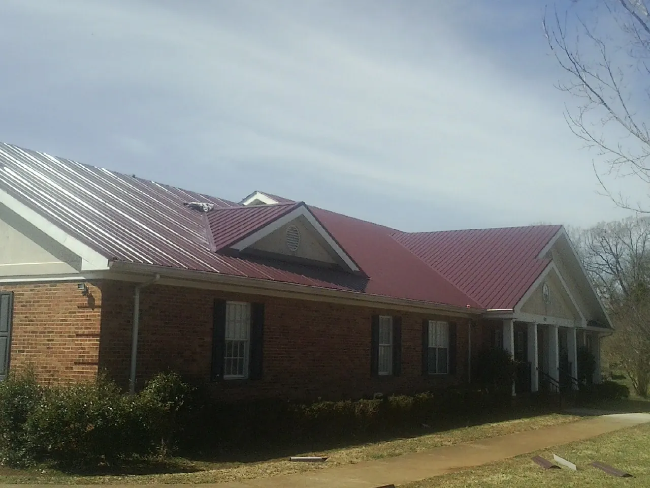 Red metal roof with gabled entries on a long brick building, from a Hail Damage Roof Repair job in Highmount