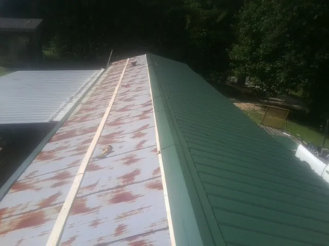 Old rusted panels beside newly installed green metal roofing — Wind Damage Roof Repair by Roofing Brothers in Highmount