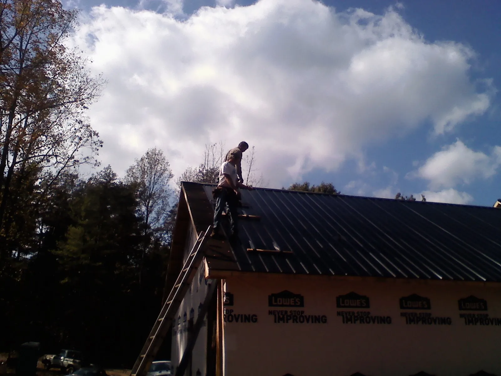 Roofer fastening dark metal panels high against a cloudy sky, from a Roof Inspection job in Highmount